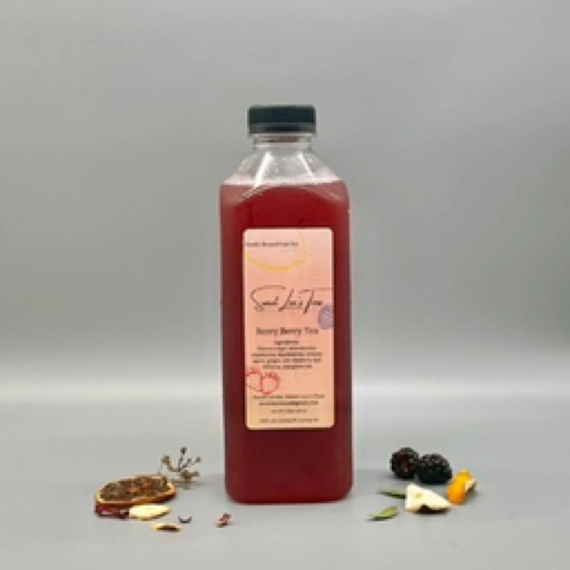 Sweet Lee’s Berry Berry Tea in a clear bottle, displayed against a neutral gray background with dried fruit slices, blackberries, and herbal ingredients scattered around.