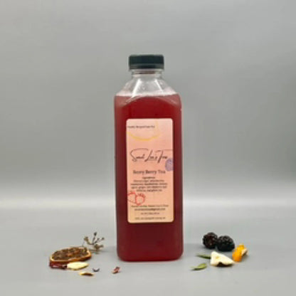 Sweet Lee’s Berry Berry Tea in a clear bottle, displayed against a neutral gray background with dried fruit slices, blackberries, and herbal ingredients scattered around.