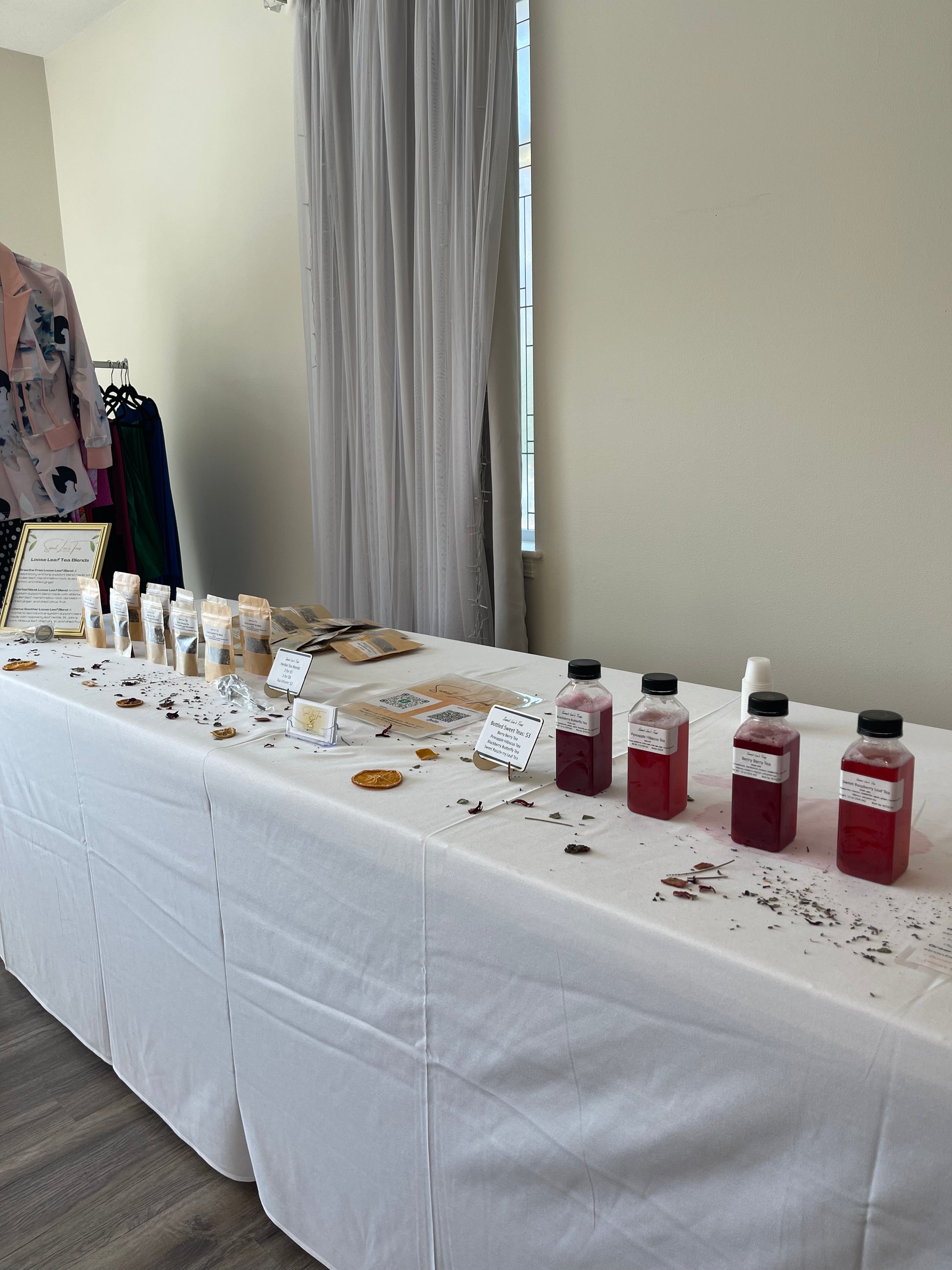 Sweet Lee’s Teas catering setup featuring bottled fruit teas and loose-leaf tea blends displayed on a white tablecloth, with dried herbs and citrus garnishes, showcasing bulk tea options for events and gatherings.