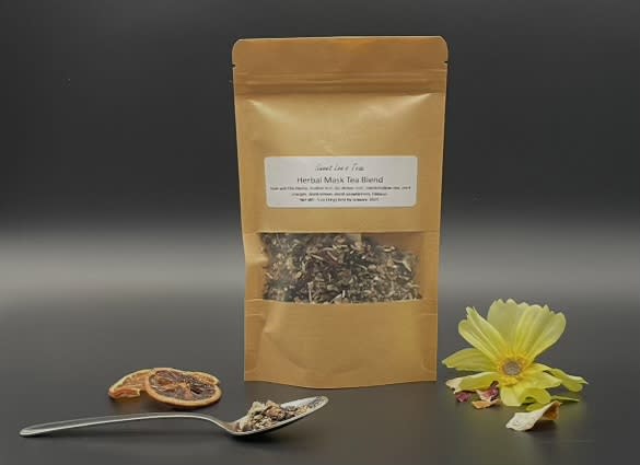 A kraft bag of Sweet Lee’s Herbal Mask Tea Blend, displayed with a spoonful of loose-leaf tea, dried citrus slices, and a yellow flower, highlighting its natural herbal ingredients and wellness benefits