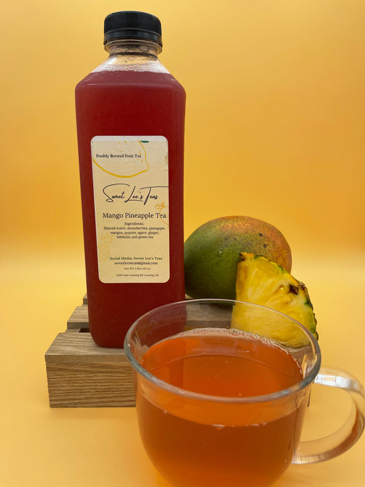 A bottle of Mango Pineapple Tea from Sweet Lee’s Teas, placed next to fresh mango and pineapple, with a cup of brewed tea in the foreground, highlighting its tropical fruit ingredients.