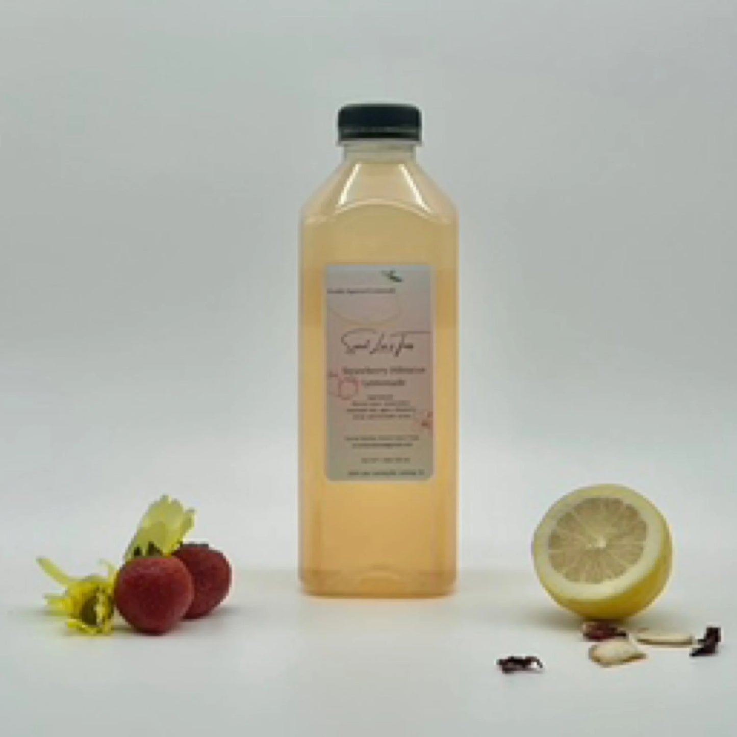 Sweet Lee’s Strawberry Hibiscus Lemonade in a clear bottle, surrounded by fresh strawberries, hibiscus petals, and a sliced lemon, highlighting its refreshing citrus and floral flavors.